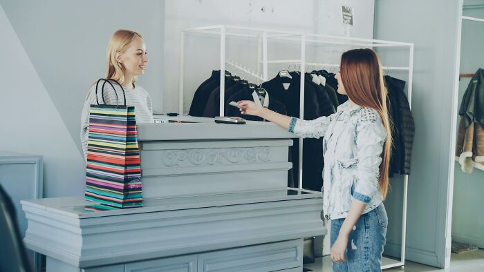 Customer at store counter with striped shopping bag, engaging with cashier, challenging beliefs on controversial opinions.