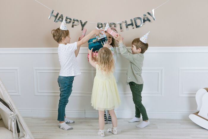 Three children in party hats exchanging a gift during a birthday celebration challenging beliefs and opinions.