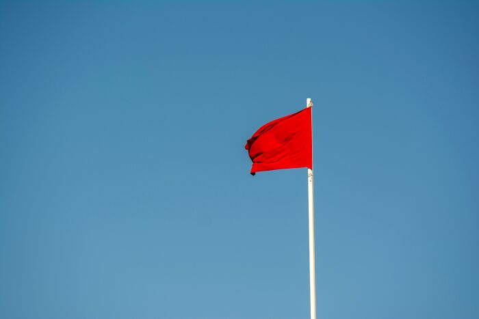 Red flag waving against clear blue sky symbolizing challenge and controversial opinions to provoke beliefs.