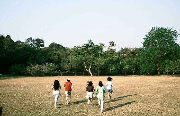 Group of young people running on a grassy field with trees, symbolizing challenge your beliefs and controversial opinions.