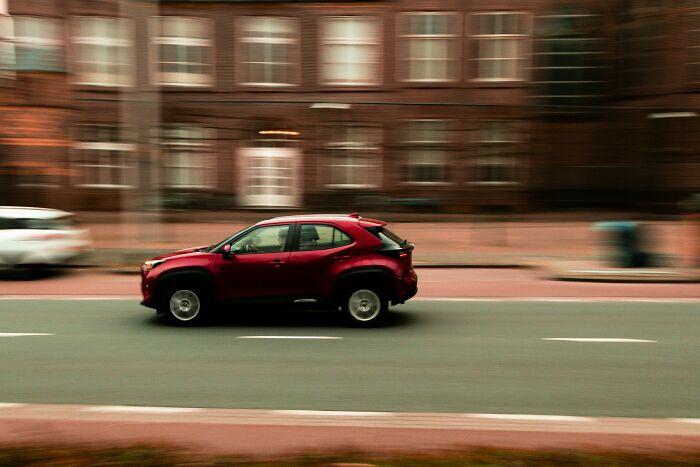 Red SUV speeding on an urban street, motion blur emphasizing dynamic movement related to challenging beliefs.