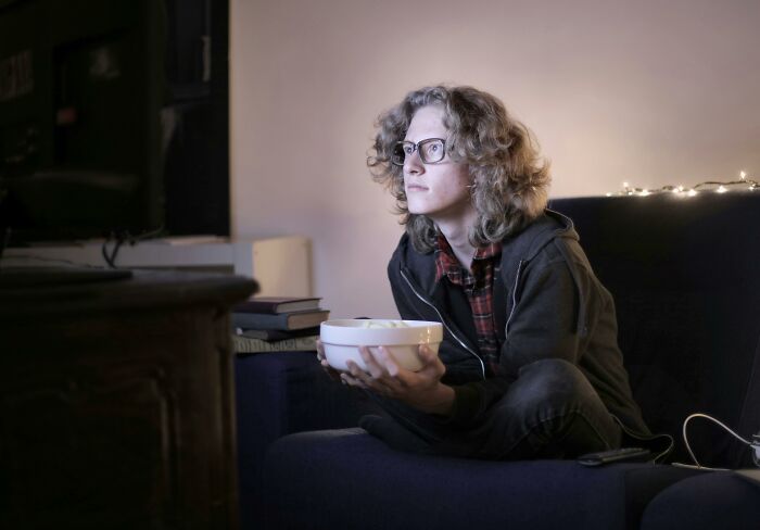 Person with glasses on a couch holding a bowl, focused and reflecting on controversial opinions and beliefs challenged.