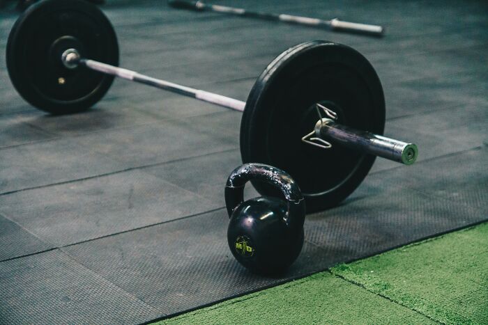 Kettlebell and barbell on gym floor representing challenge your beliefs in fitness and strength training opinions