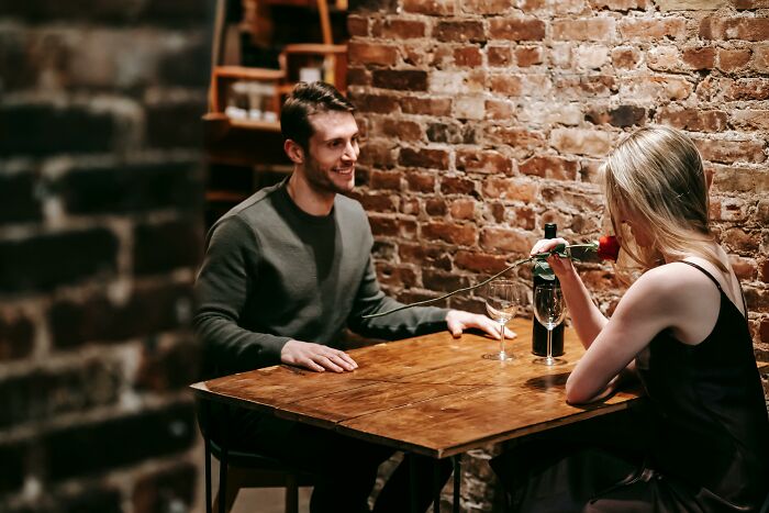 Couple having a conversation in a cozy setting, challenging their beliefs over wine and a rose on the table.