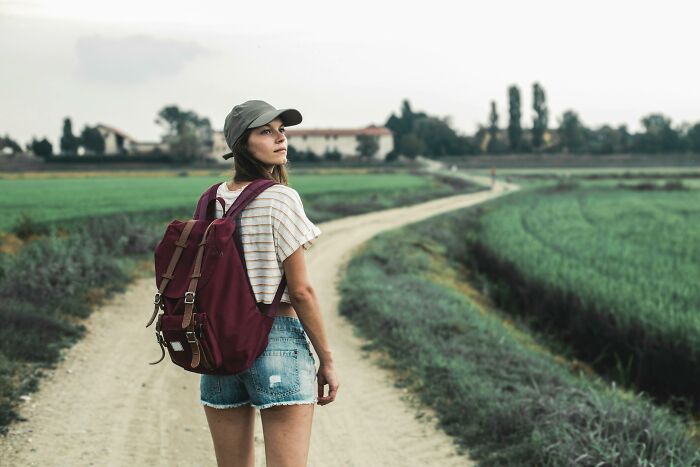 Young woman with backpack standing on a rural path, symbolizing challenge your beliefs and controversial opinions journey.