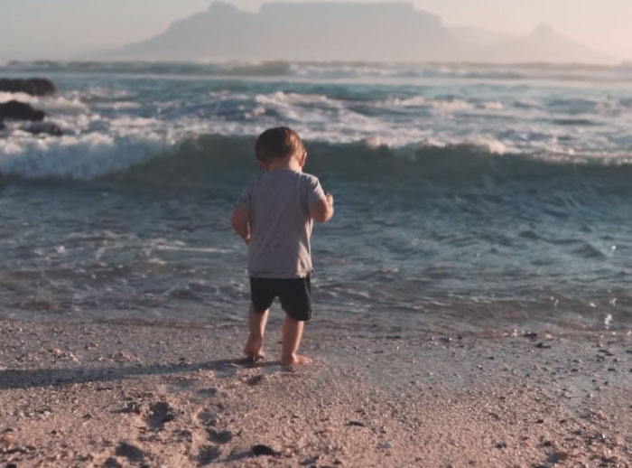Toddler standing alone on beach shore with waves, evoking unsettling mysteries and intriguing natural scenes.
