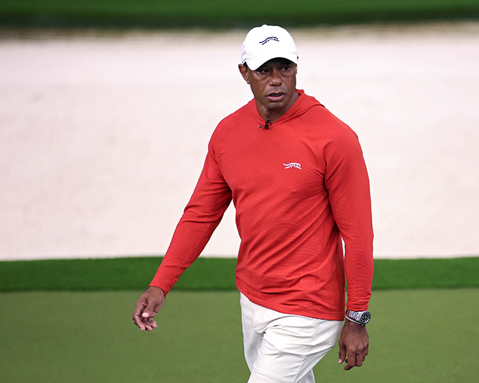Tiger Woods wearing a red shirt and white cap on a golf course during a sporting event.