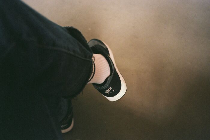 Person wearing black Nike sneakers and white socks sitting with legs crossed on a concrete floor, illustrating dumb ER visit scenario.