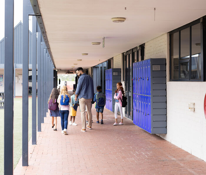 Middle school hallway with students and an adult near blue lockers under covered walkway at school.