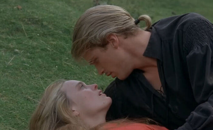 A couple lying closely on grass, sharing an intimate moment reflecting unconventional family traditions.