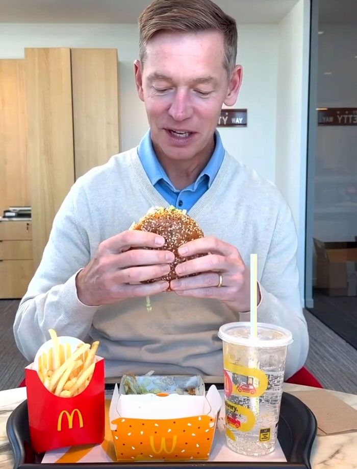 Man holding a burger with McDonald's fries and drink on table, related to burger battle and fast food brands.