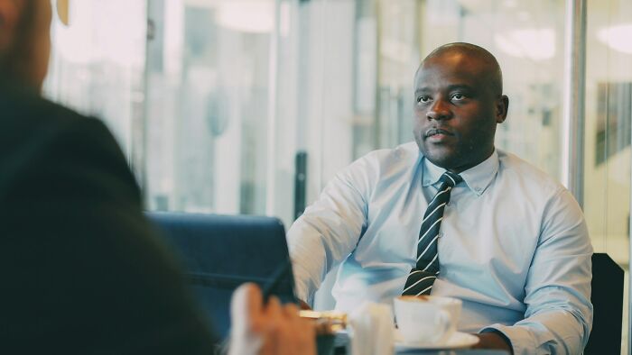 Man in shirt and tie experiencing culture shock during a serious conversation in a modern office setting.