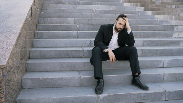 Man in a black suit sitting on outdoor concrete steps looking confused, illustrating bizarre true stories concept