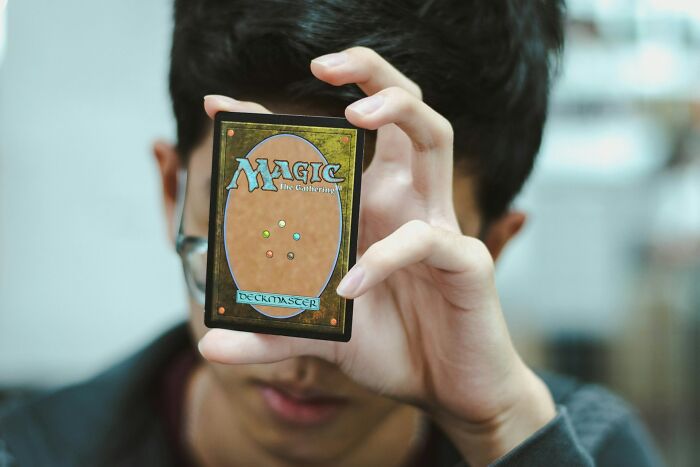 Person holding a Magic the Gathering card close to face, symbolizing shaky industries vulnerable to collapse exposure.