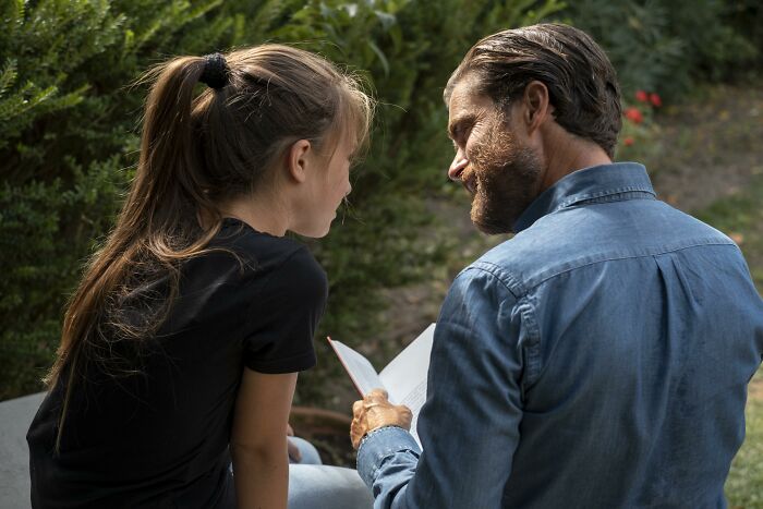 Man and woman outdoors, man appears to be mansplaining as they look at a book, capturing mansplaining interaction.