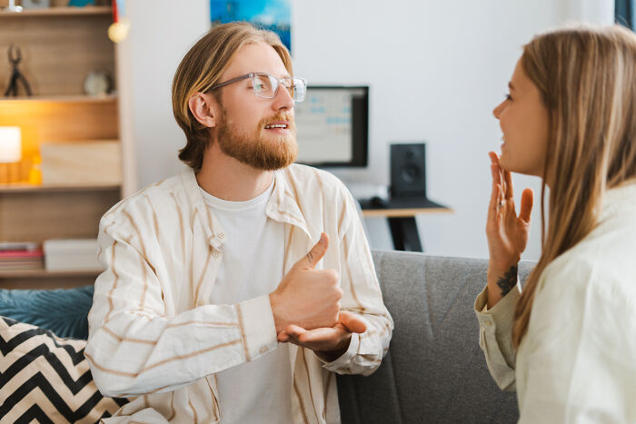 Man explaining something with gestures to a woman in a living room, illustrating mansplaining behavior.