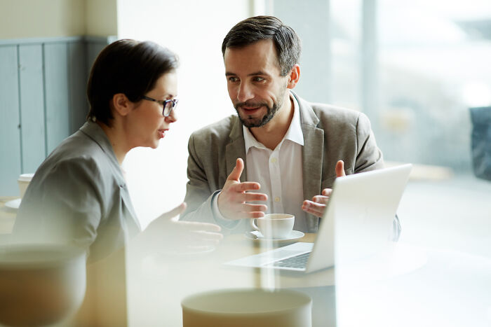 Man explaining something to a woman during a business meeting, illustrating mansplaining in a professional setting.