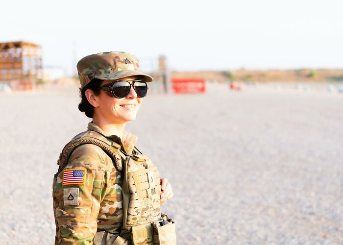 Female soldier in camouflage uniform and sunglasses smiling outdoors, illustrating confidence beyond mansplaining moments.