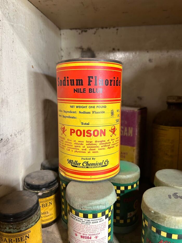 Old can of sodium fluoride poison with bright red and yellow label among other vintage containers in old home cabinet.