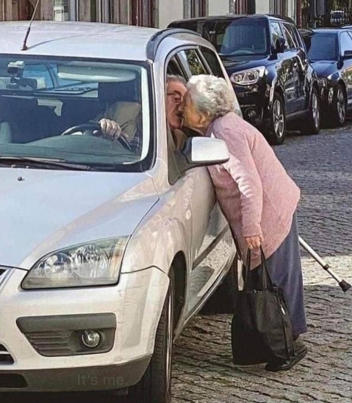 Elderly couple sharing a tender kiss through a car window, showing uplifting moments of love and kindness.