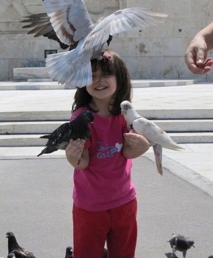 Smiling child holding and surrounded by pigeons outdoors, capturing uplifting moments of kindness in the world.