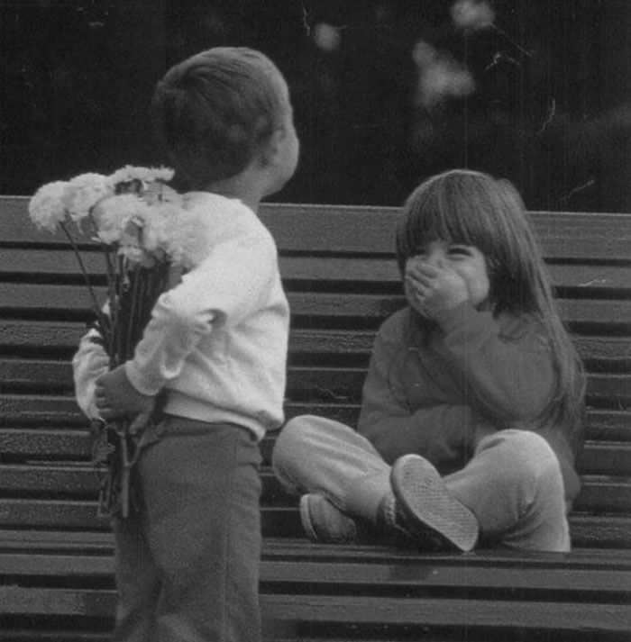 Two children on a bench with boy hiding flowers behind his back and girl smiling, capturing uplifting moments in the world.
