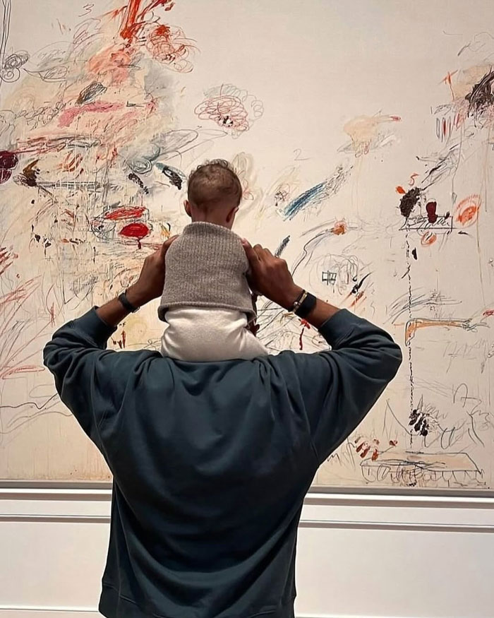 Man holding a baby on his shoulders looking at abstract art, representing uplifting moments and good left in the world.