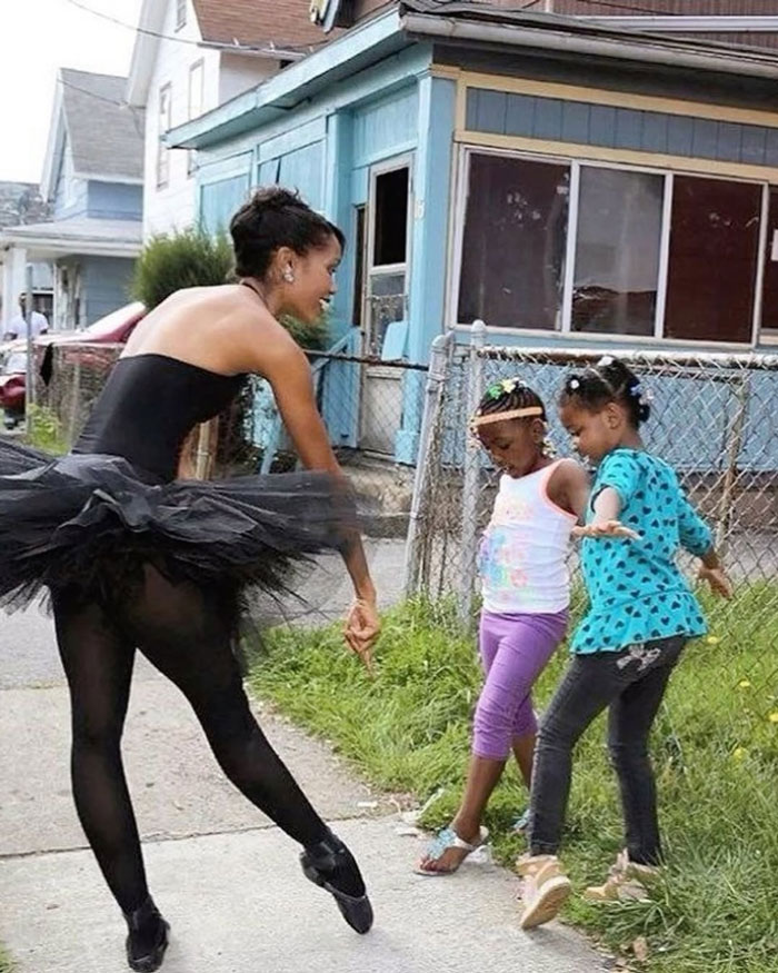 Ballerina dancing joyfully with two young girls on a neighborhood sidewalk, spreading uplifting moments and positivity.