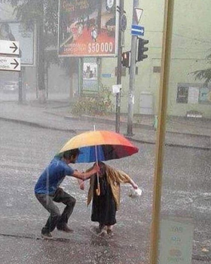 Man holding colorful umbrella over woman in rain, showing uplifting moments and good left in the world.