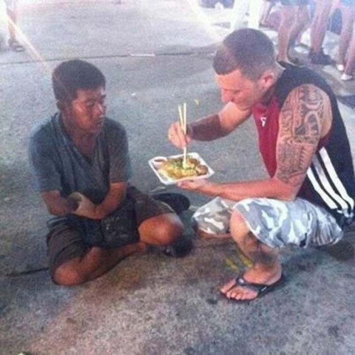 Man offering food with chopsticks to a homeless person sitting on the ground, showing acts of kindness and uplifting moments.