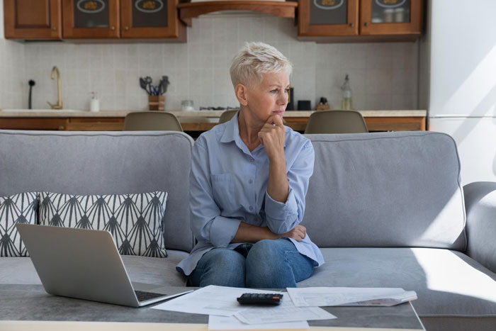 Woman sitting on couch looking concerned, surrounded by bills and laptop, reflecting homemaker laments about adult kids.