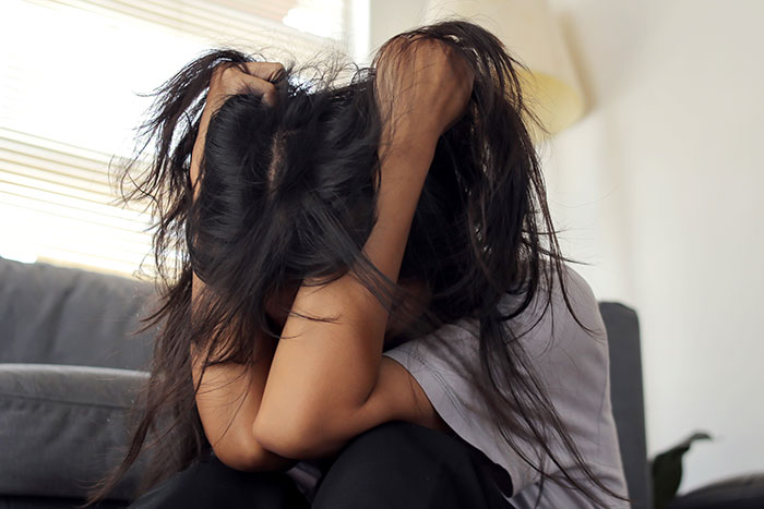 Woman sitting with hands tangled in long hair, frustrated and stressed dealing with lice treatment refusal.
