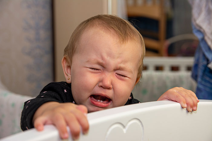 Crying baby in a crib with a distressed expression, illustrating chaos after a long shift at home.