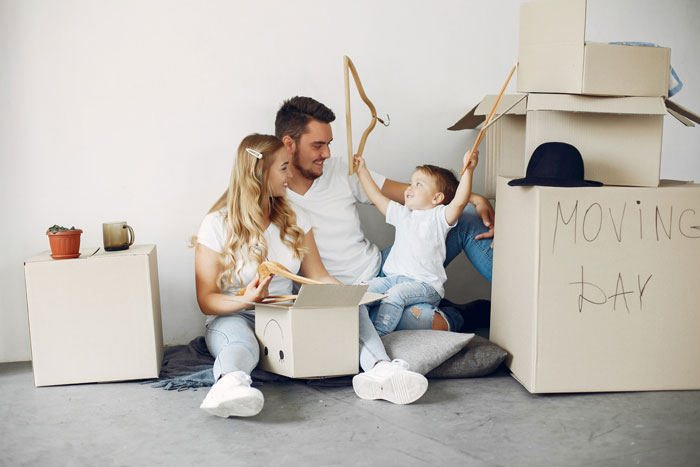 Young family with toddler sitting on floor surrounded by moving boxes, highlighting grandparents kicking family out conflict.