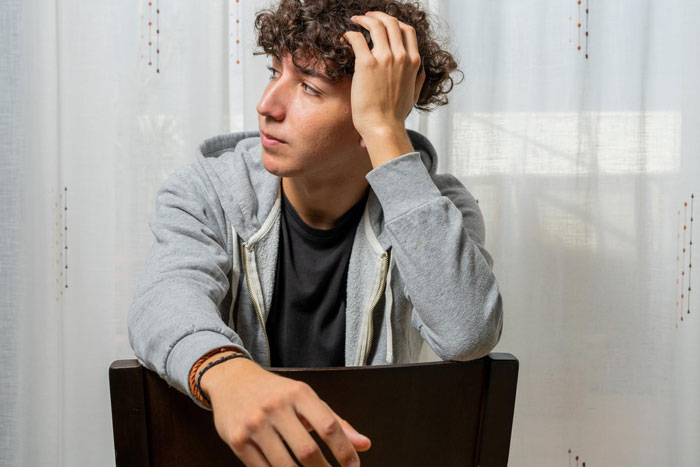 Young man in a gray hoodie looking concerned, illustrating family conflict over toddler and medical school decisions.