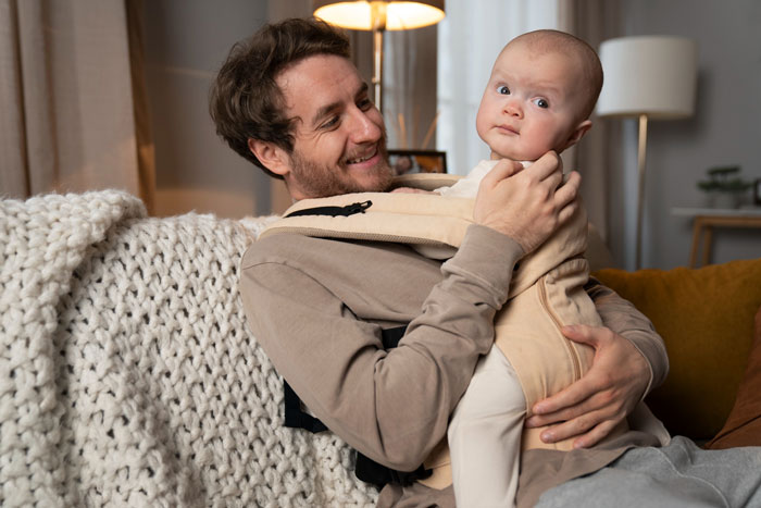 Man holding baby in a carrier at home illustrating a woman&rsquo;s confession about a surprise baby trap to keep her boyfriend.