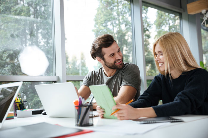 Man and woman discussing tablet and documents at a bright workspace, reflecting on relationship and marriage concerns.