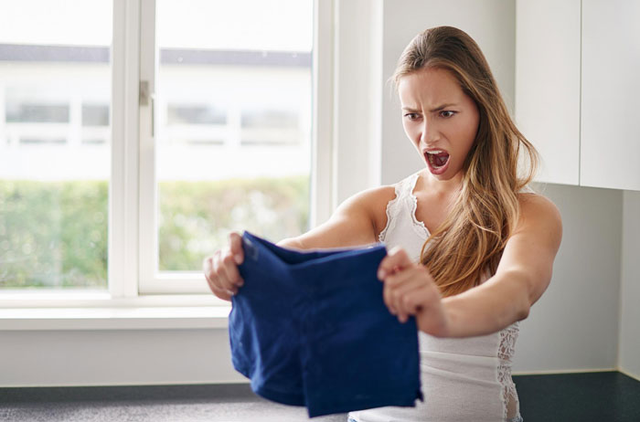 Woman showing anger while holding blue shorts indoors, depicting toxic wife behavior in a Zoom conflict with teacher hubby.