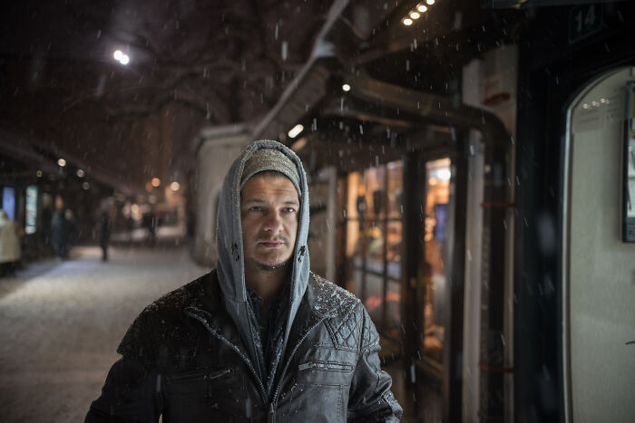 Man in a hooded jacket standing alone in a snowy, dimly lit urban area, evoking a sense of scary encounters.