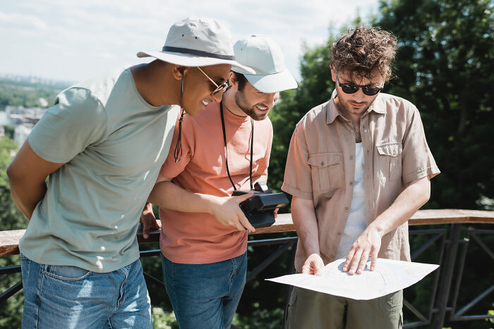 Three men outdoors studying a map and camera during a hiking trip, evoking curiosity linked to scary encounters alone.