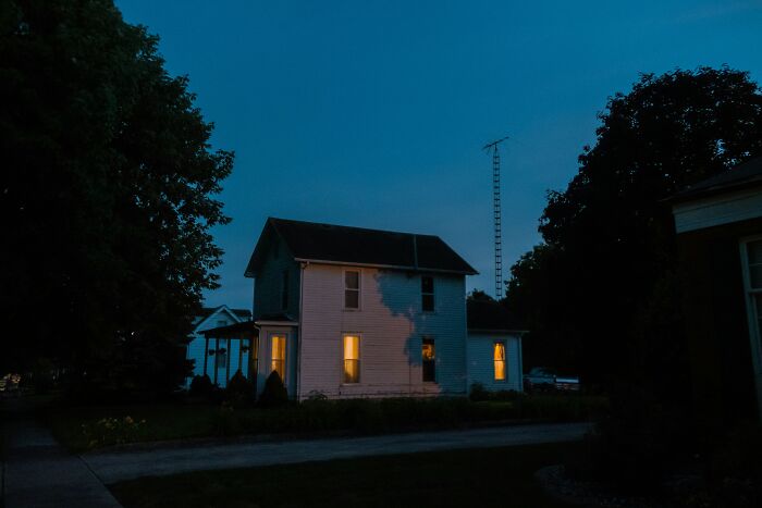 A white house with warm lights glowing inside at night, evoking a sense of eerie and scary encounters alone.
