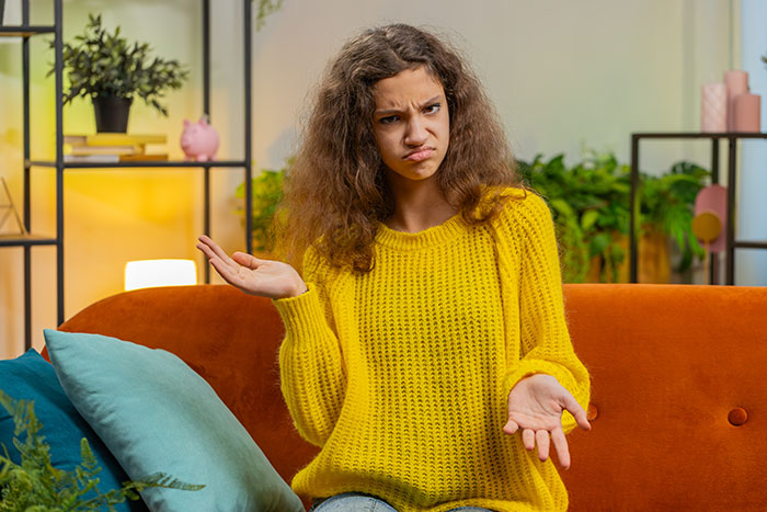 Young woman in yellow sweater looking confused on a sofa, representing drama over Midol and tampons stashed in bathroom.