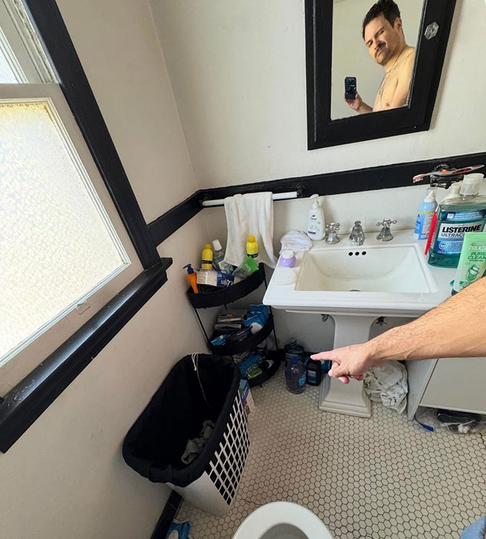 Man pointing inside a bathroom corner with Midol and tampons stashed for friends, causing guest drama over virtue signaling.