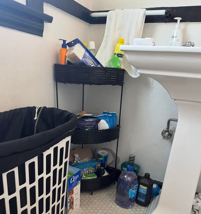 Bathroom shelf with Midol and tampons stocked for guests, next to a laundry basket and a white pedestal sink.