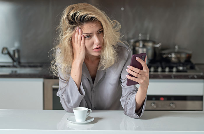 Woman looking stressed while using phone, reflecting drama and self-absorption in a tense personal situation.