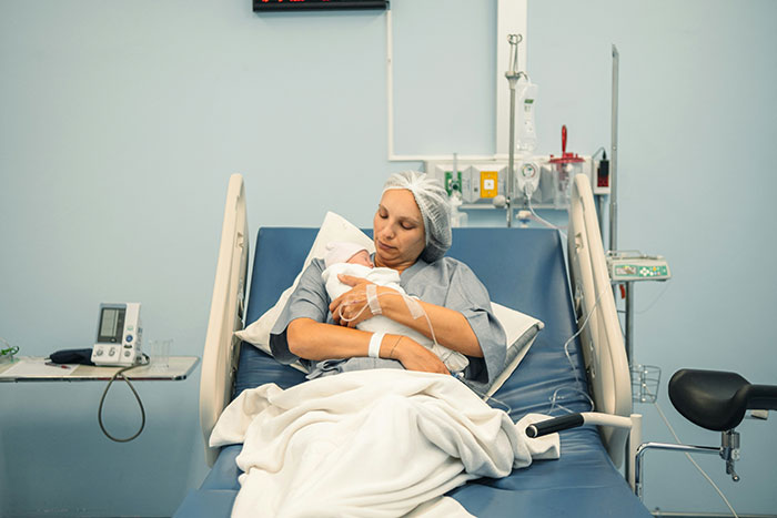Woman in hospital bed holding newborn baby, representing family drama and self-absorption themes.