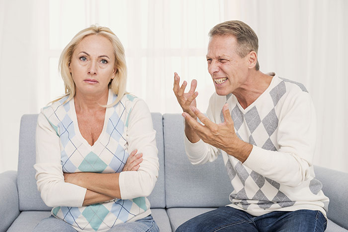 Man and woman in a tense argument, man displaying breakup drama while woman looks upset and disengaged.