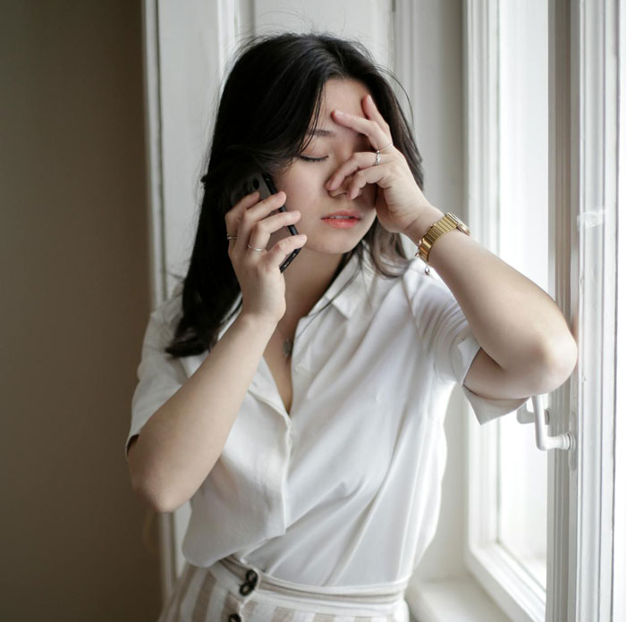 Woman upset while talking on phone near window, reflecting emotions related to boyfriend and pregnant mistress situation.