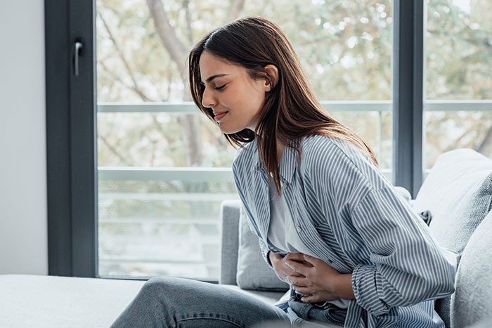 Pregnant woman sitting on a couch, holding her stomach and appearing to be in labor inside a bright living room.
