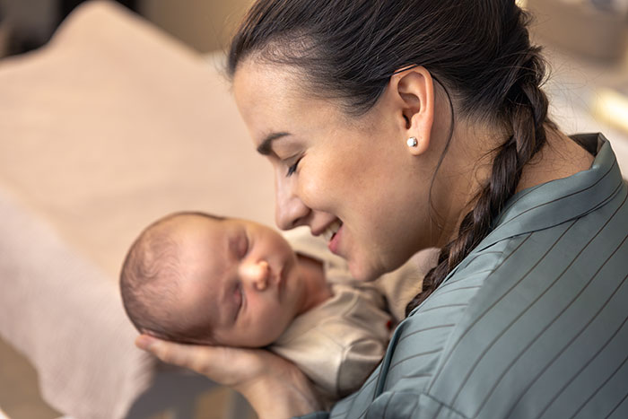 Mother smiling and holding newborn baby close, celebrating pregnancy and labor moments with joy and tenderness.